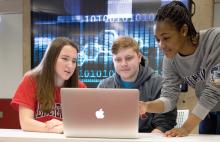Three students around a laptop