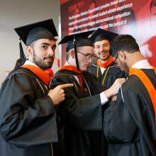 Students in their cap and gowns help each other fix their robes